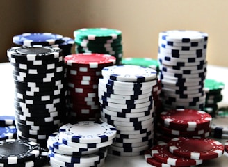 Stacks of colorful poker chips are arranged in piles on a white surface. The chips are blue, red, green, black, and white, each color having distinct markings.