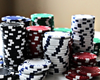 Stacks of colorful poker chips are arranged in piles on a white surface. The chips are blue, red, green, black, and white, each color having distinct markings.