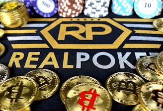 Stacks of poker chips in various colors are arranged in the background, while in the foreground, there are numerous golden coins featuring the Bitcoin symbol. The text 'REALPOKER' is prominently displayed in gold and silver lettering on a dark background.