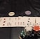 A poker game setup is displayed, featuring stacks of colorful poker chips including red, green, black, and white. Playing cards are laid out in a row, revealing various suits and numbers. Three distinct dealer buttons labeled 'DEALER', 'LITTLE BLIND', and 'BIG BLIND' are positioned above the card lineup.
